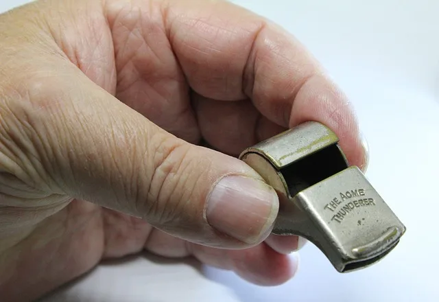 Dłoń trzymająca gwizdek jako symbol zgłaszania nieprawidłowości przez sygnalistę